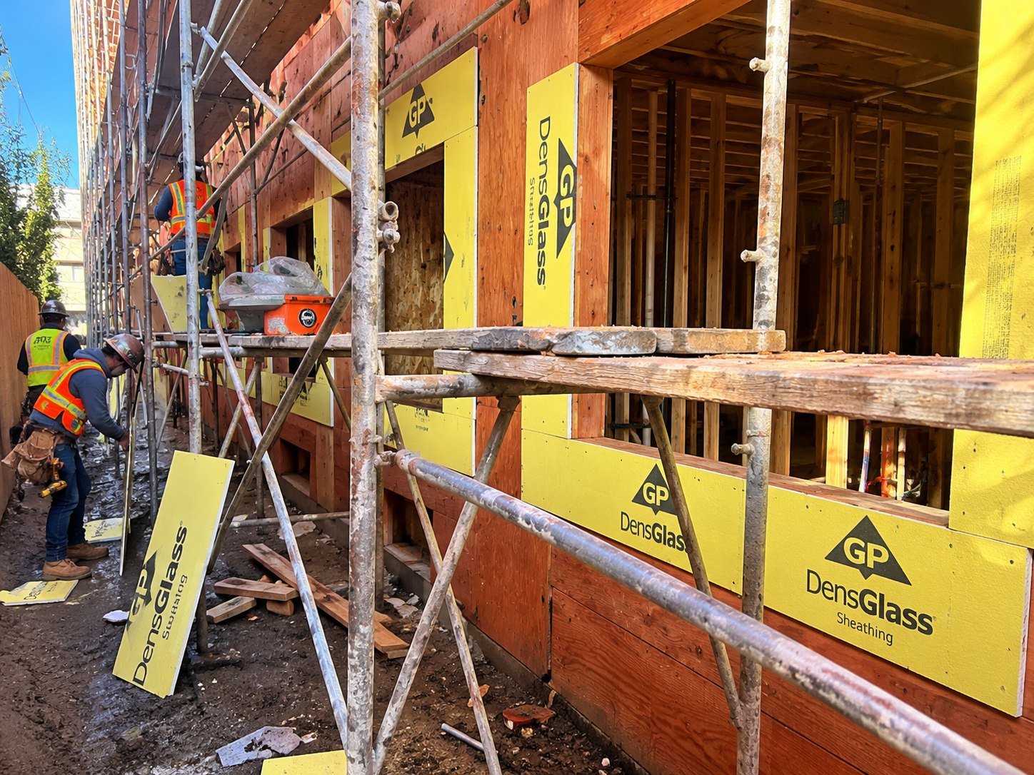 Exterior DensGlass sheathing installation along a scaffold walkway