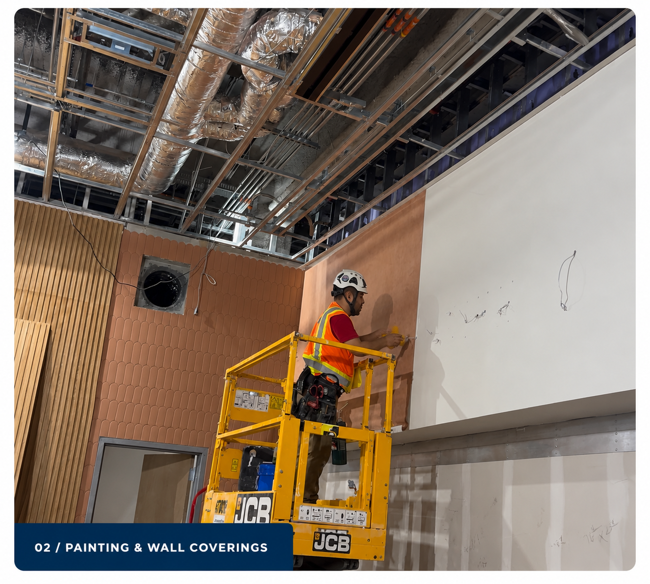 PDG worker applying wall covering finish from a scissor lift inside a commercial construction site